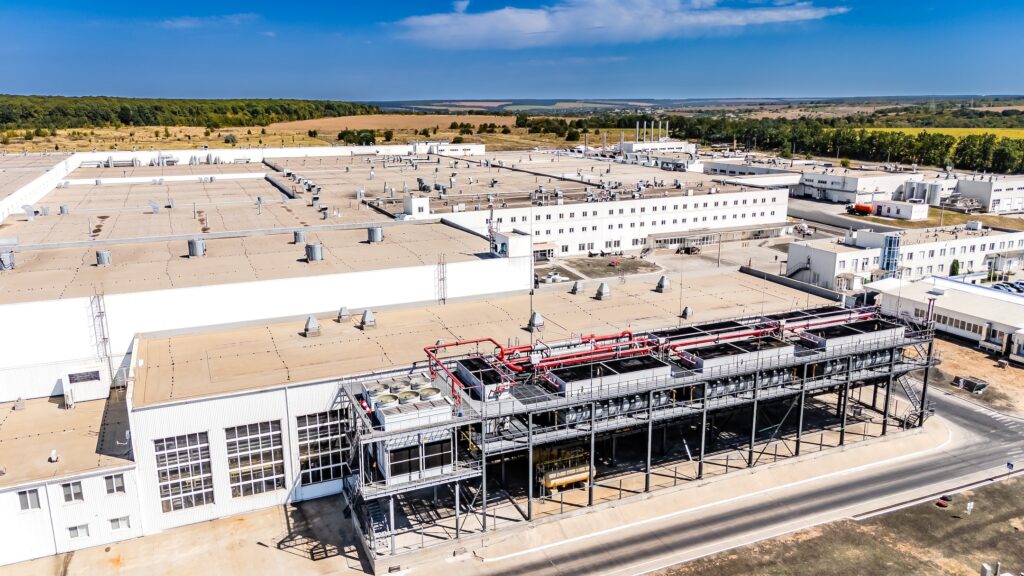 Industrial cooling towers and HVAC systems on factory roof. Detailed view of mechanical cooling equipment and ventilation systems on top of a white industrial building.
