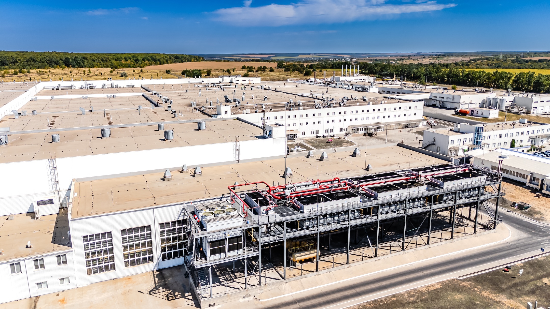Industrial cooling towers and HVAC systems on factory roof. Detailed view of mechanical cooling equipment and ventilation systems on top of a white industrial building.
