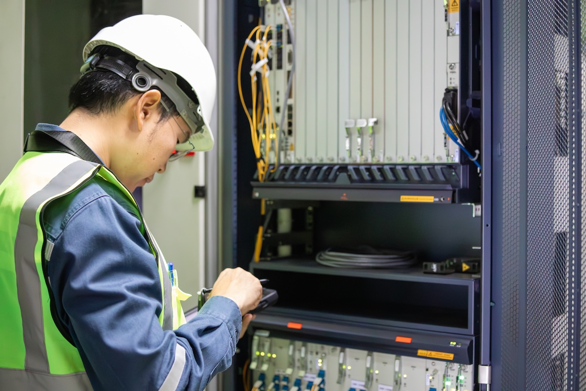 Network technician performing inspection on server equipment with safety helmet and vest in data center