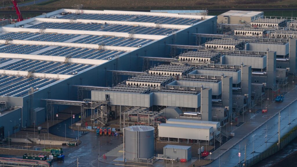 Large industrial facility featuring a data center building with rooftop solar panels, rows of integrated cooling systems, and critical infrastructure for sustainable technology operations