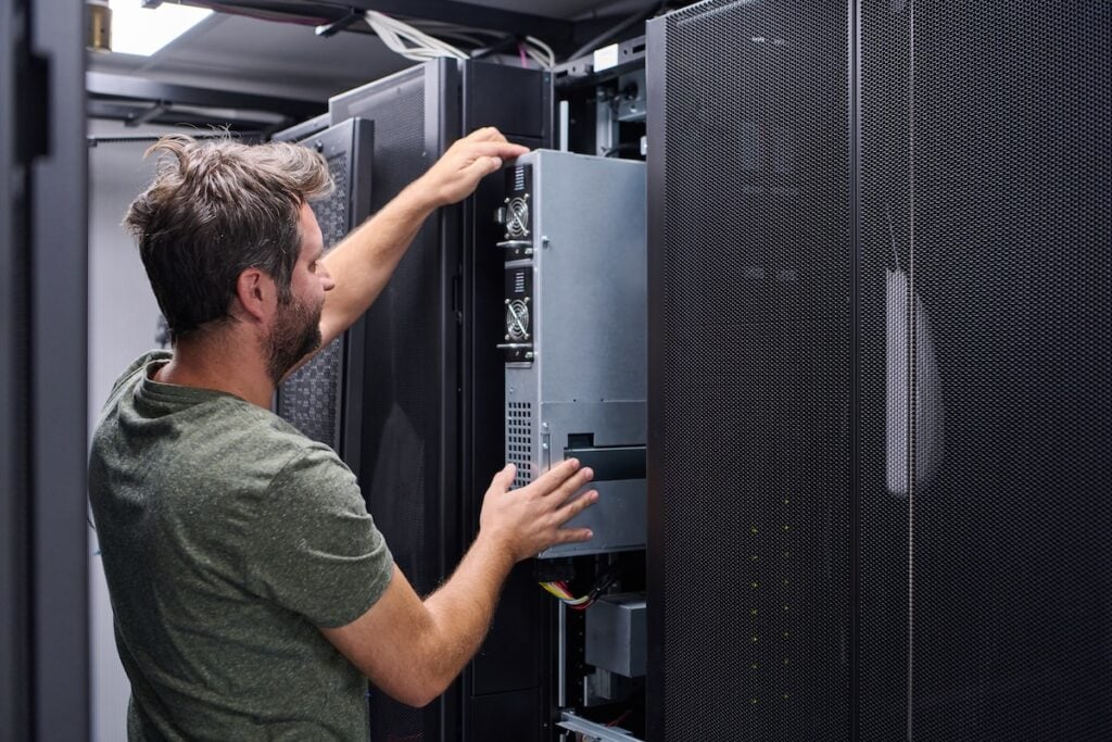 IT technician installing server hardware in a data center rack performing maintenance and configuration