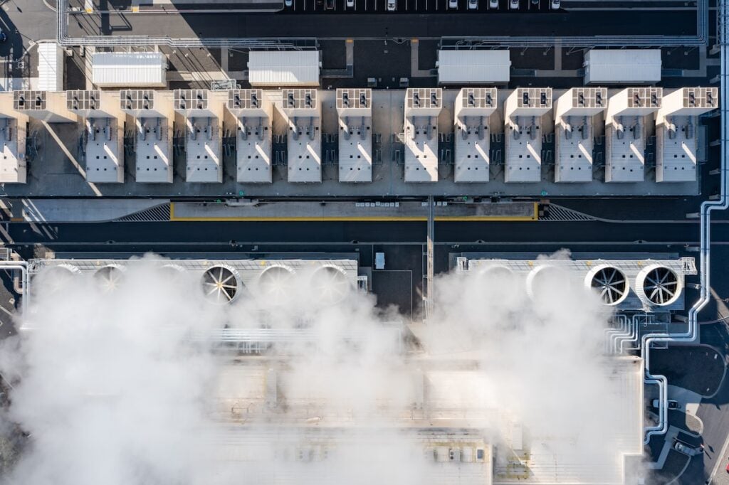 Aerial drone view of large data center cooling systems with industrial fans and steam rising from rooftop infrastructure in The Dalles, Oregon, USA supporting cloud computing and digital technology