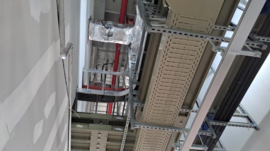 complex industrial ceiling infrastructure with cable trays and insulated piping in a data center