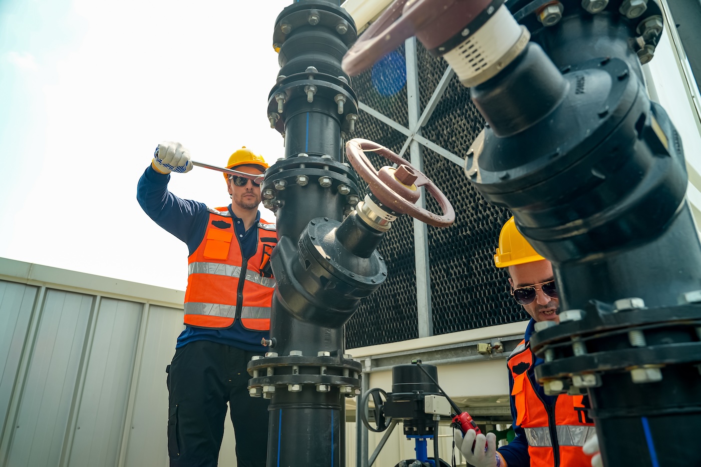 Industrial workers in safety vests and hard hats performing maintenance on large pipes