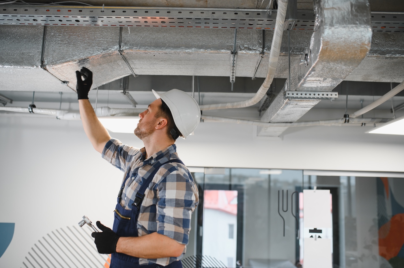 Hvac technician inspecting metal air ducts during installation of ventilation system in a building under construction